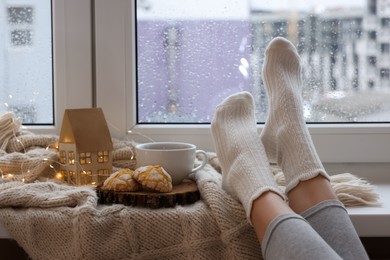 Woman in knitted socks relaxing near window at home, closeup. Space for text