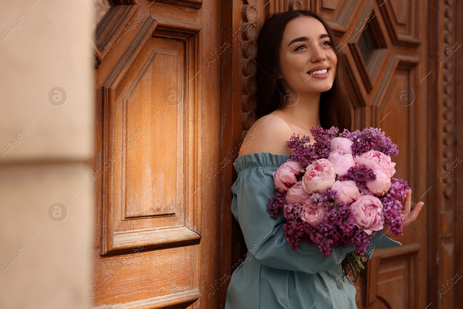 Photo of Beautiful woman with bouquet of spring flowers near building outdoors, space for text