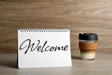 Notebook with word Welcome and cup of coffee on table