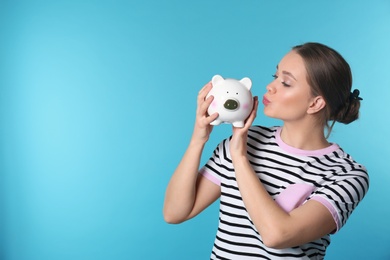 Photo of Happy young woman with piggy bank and space for text on color background. Money saving