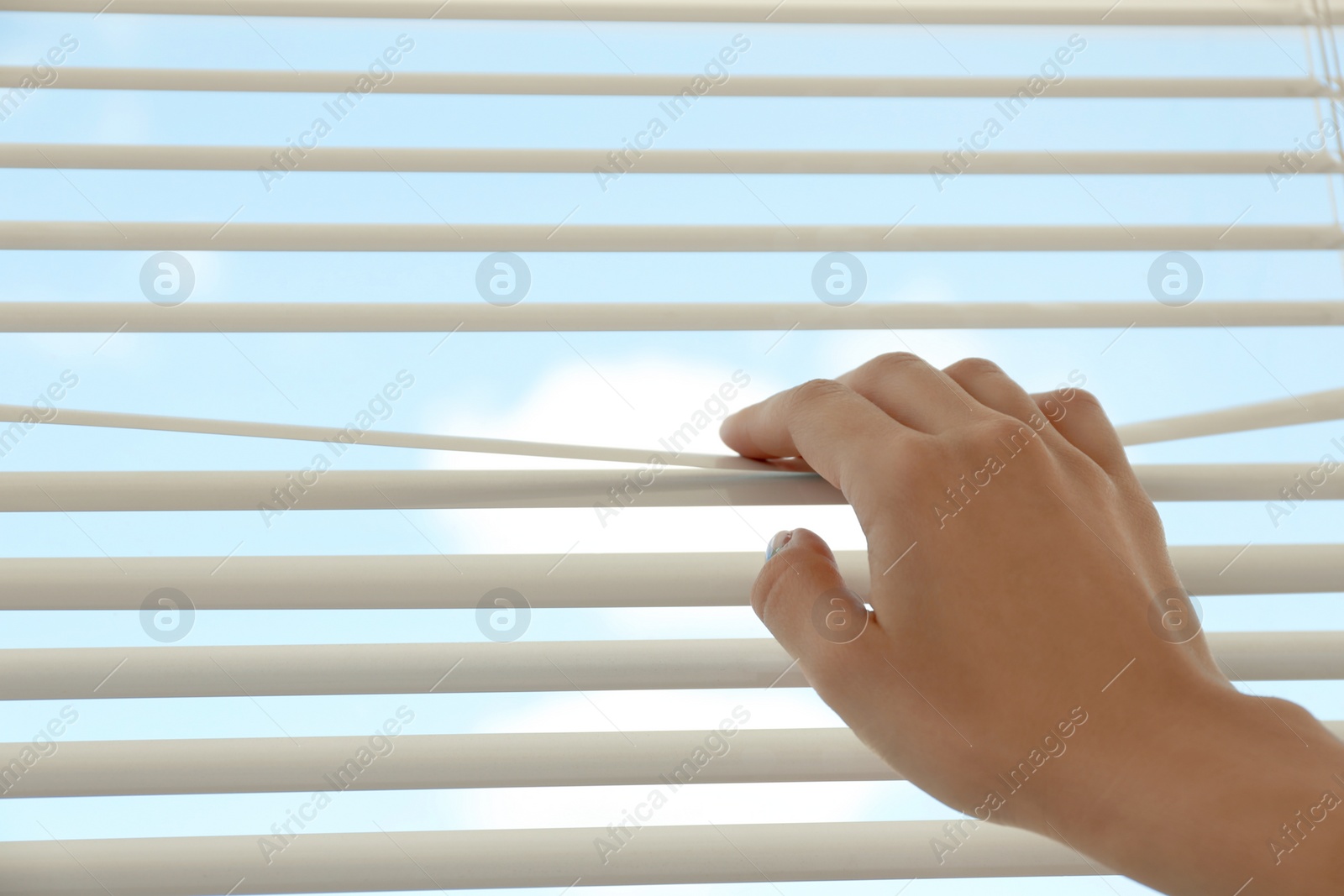 Photo of Woman opening horizontal window blinds at home, closeup. Space for text