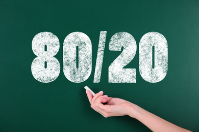 Image of Pareto principle concept. Woman writing 80/20 on chalkboard, closeup