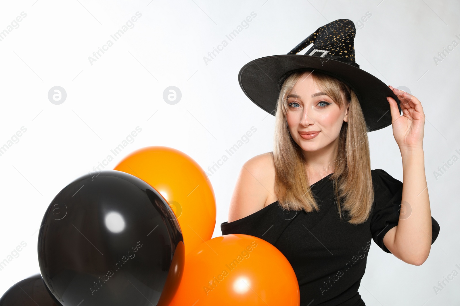 Photo of Beautiful woman in witch costume with balloons on white background. Halloween party