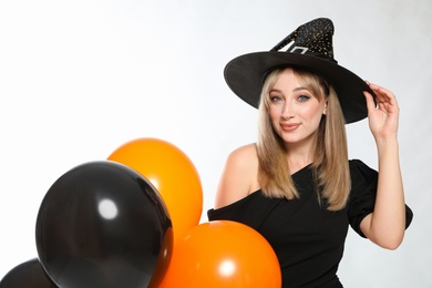 Beautiful woman in witch costume with balloons on white background. Halloween party