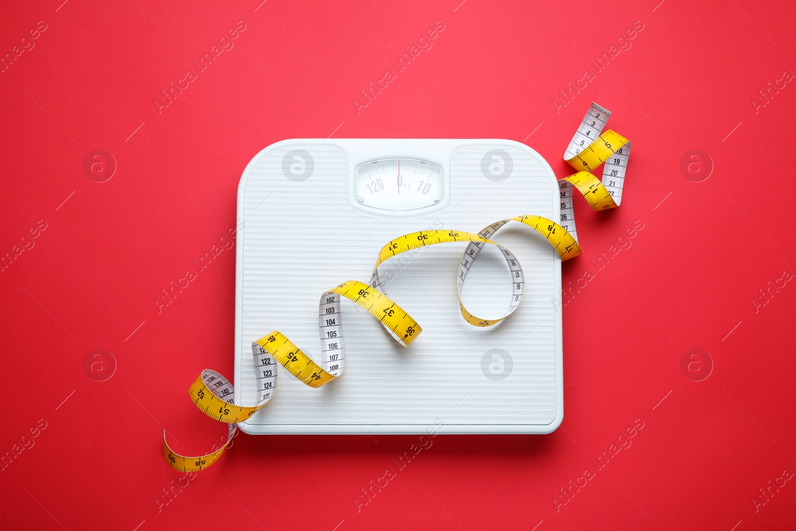 Photo of Scales and measuring tape on red background, top view