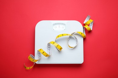 Scales and measuring tape on red background, top view