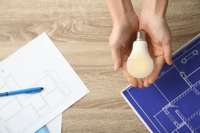 Photo of Woman holding lamp bulb over table with documents, top view