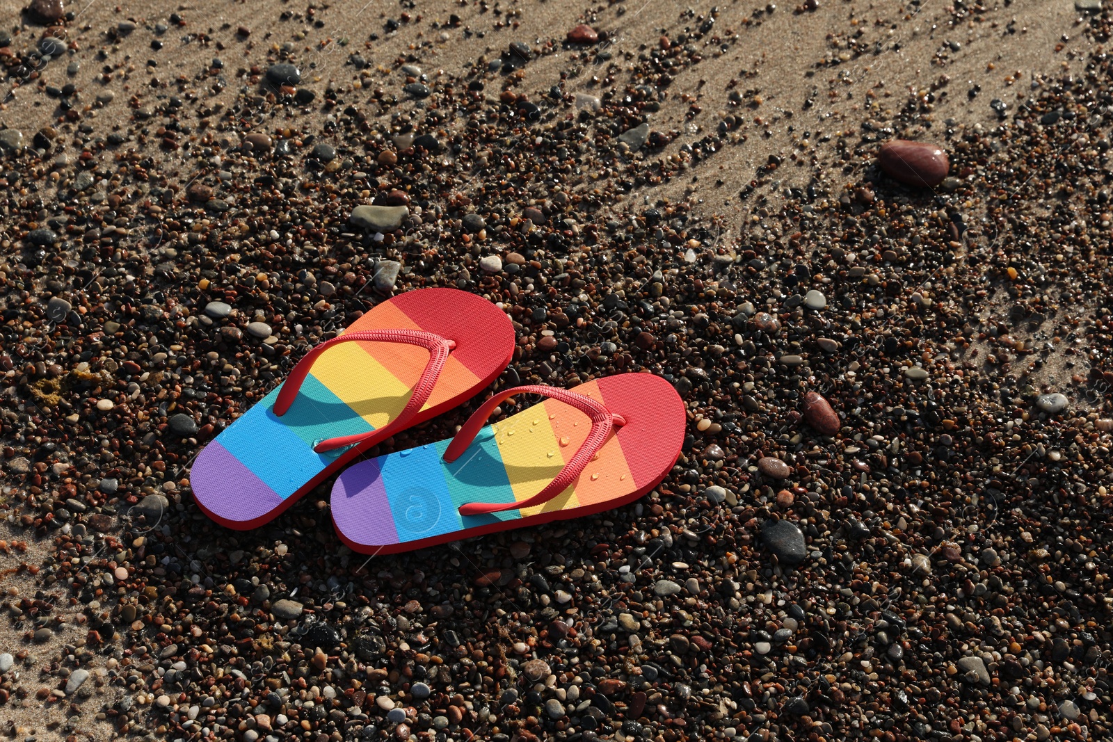 Photo of Stylish rainbow flip flops on pebbles at beach, above view. Space for text