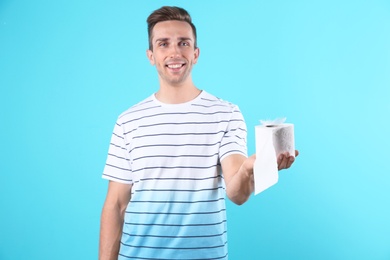 Photo of Young man holding toilet paper roll on color background