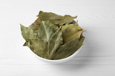 Photo of Bay leaves in bowl on white wooden table, closeup