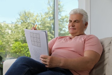 Senior man solving sudoku puzzle on sofa at home