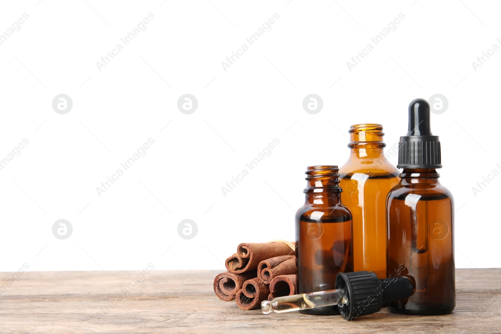 Photo of Bottles of essential oils and cinnamon sticks on wooden table against white background. Space for text