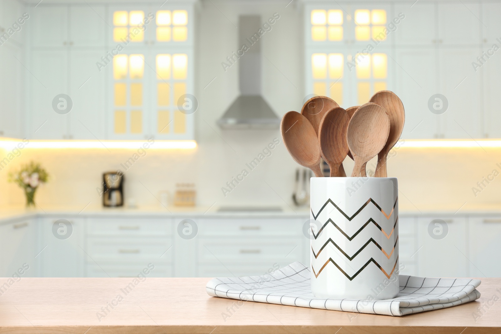 Image of Holder with spoons on wooden table and blurred view of stylish kitchen interior. Mockup for design