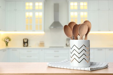 Holder with spoons on wooden table and blurred view of stylish kitchen interior. Mockup for design