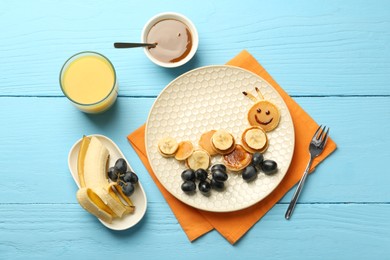 Photo of Creative serving for kids. Plate with cute caterpillar made of pancakes, grapes and banana on light blue wooden table, flat lay