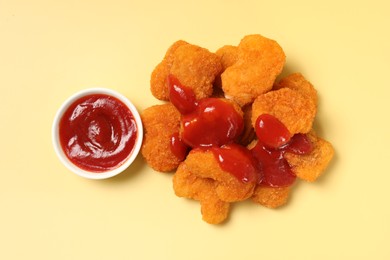 Photo of Tasty chicken nuggets with ketchup on pale yellow background, flat lay