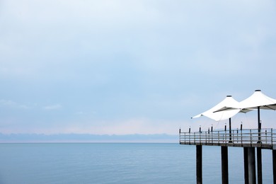 Photo of Beautiful view of pier with beach umbrellas near sea. Space for text