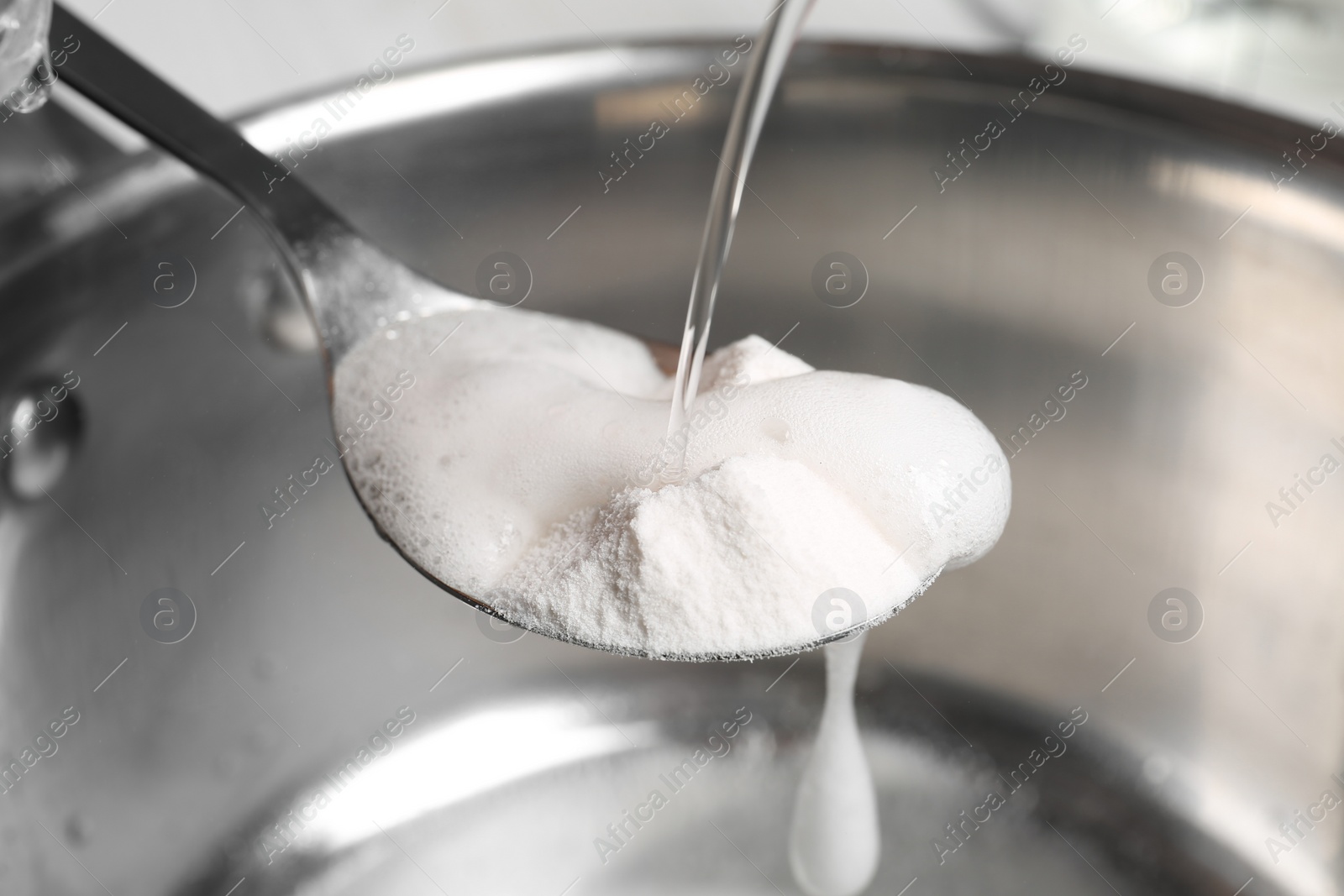 Photo of Pouring vinegar into spoon with baking soda over saucepan, closeup