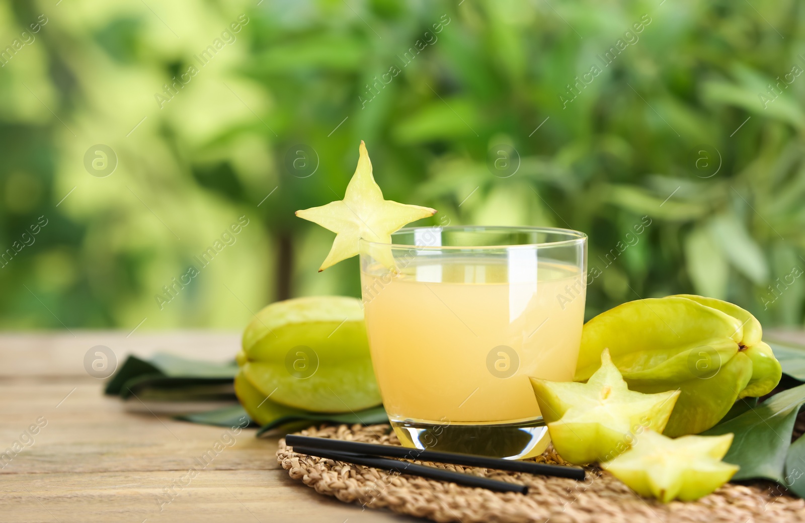 Photo of Delicious carambola juice and fresh fruits on wooden table against blurred background. Space for text