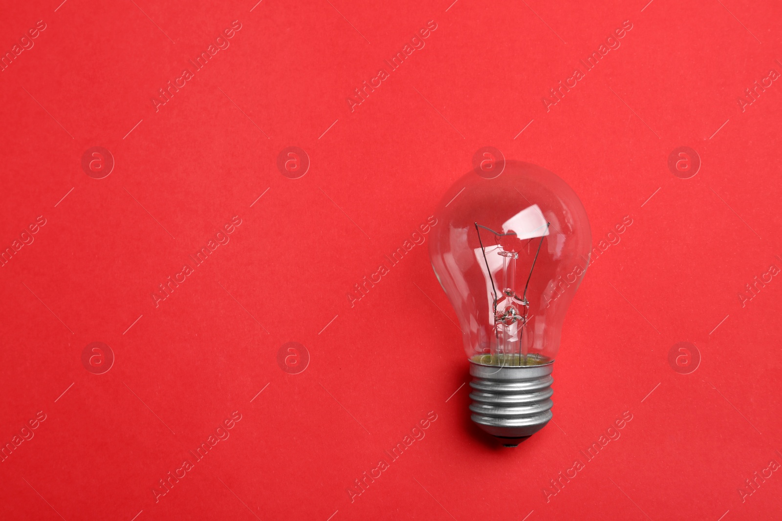 Photo of New incandescent lamp bulb on red background, top view. Space for text