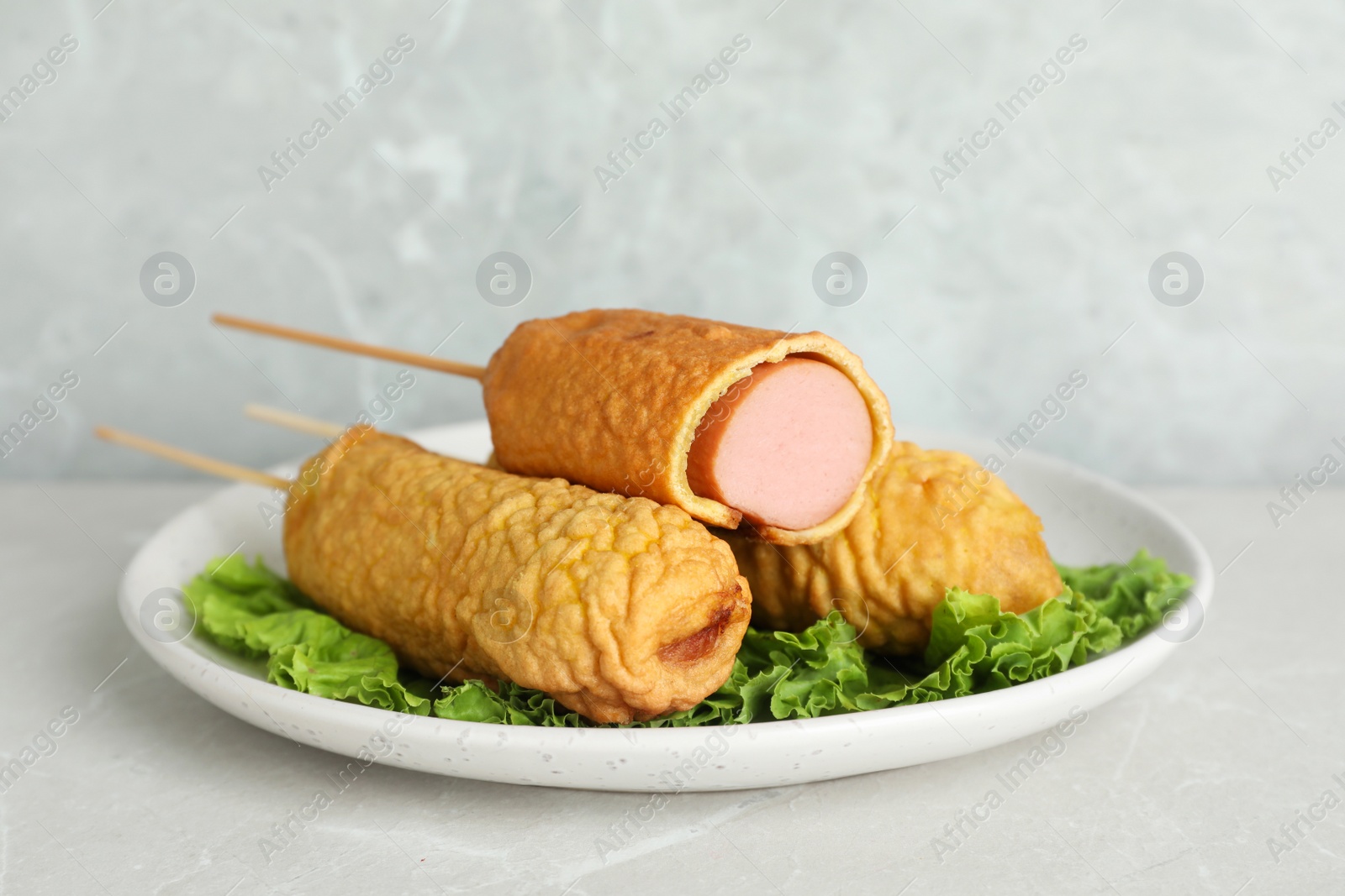 Photo of Delicious corn dogs with lettuce on light table