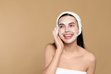 Happy young woman washing face with cosmetic product on beige background, space for text