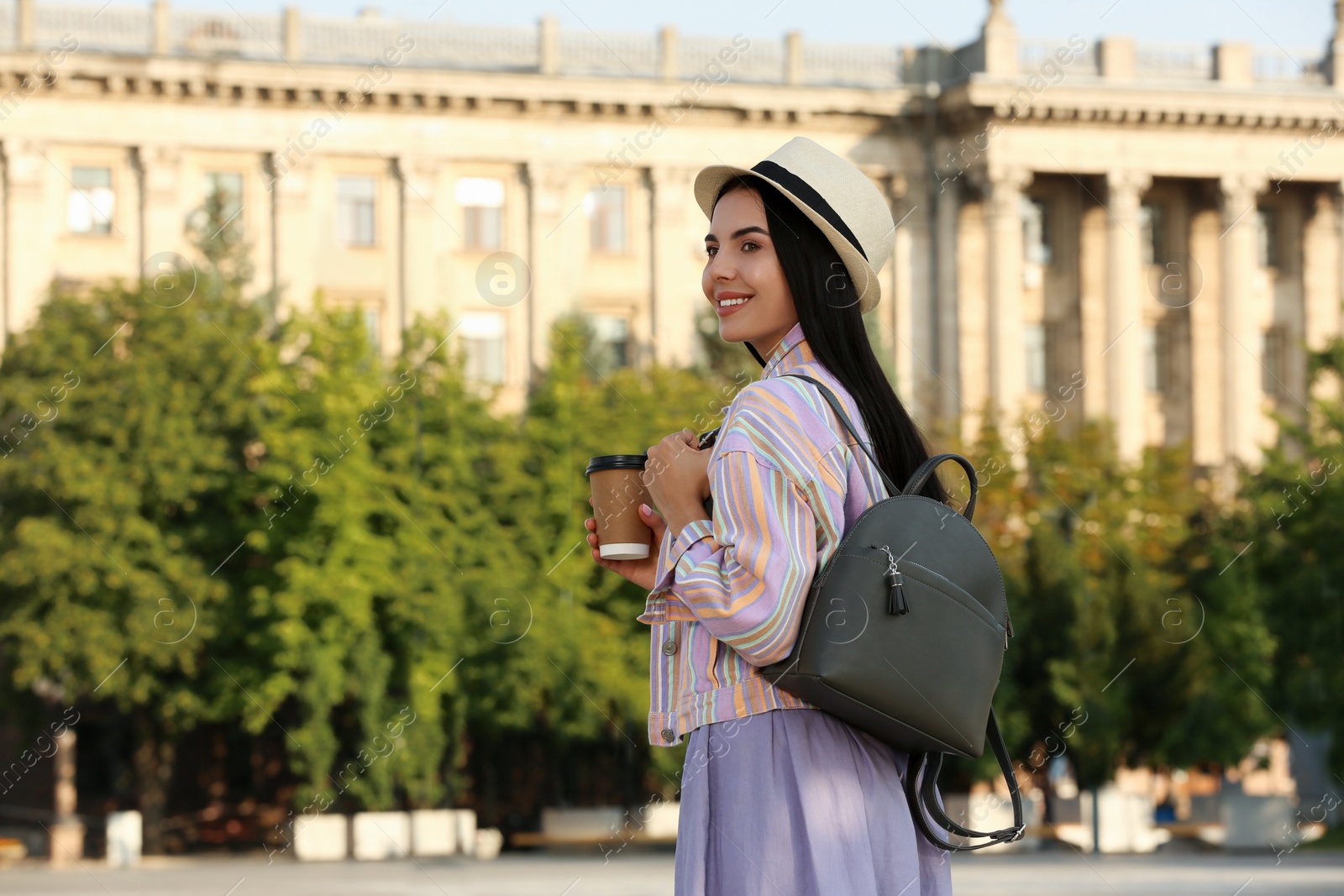 Photo of Beautiful young woman with stylish black backpack and coffee on city street