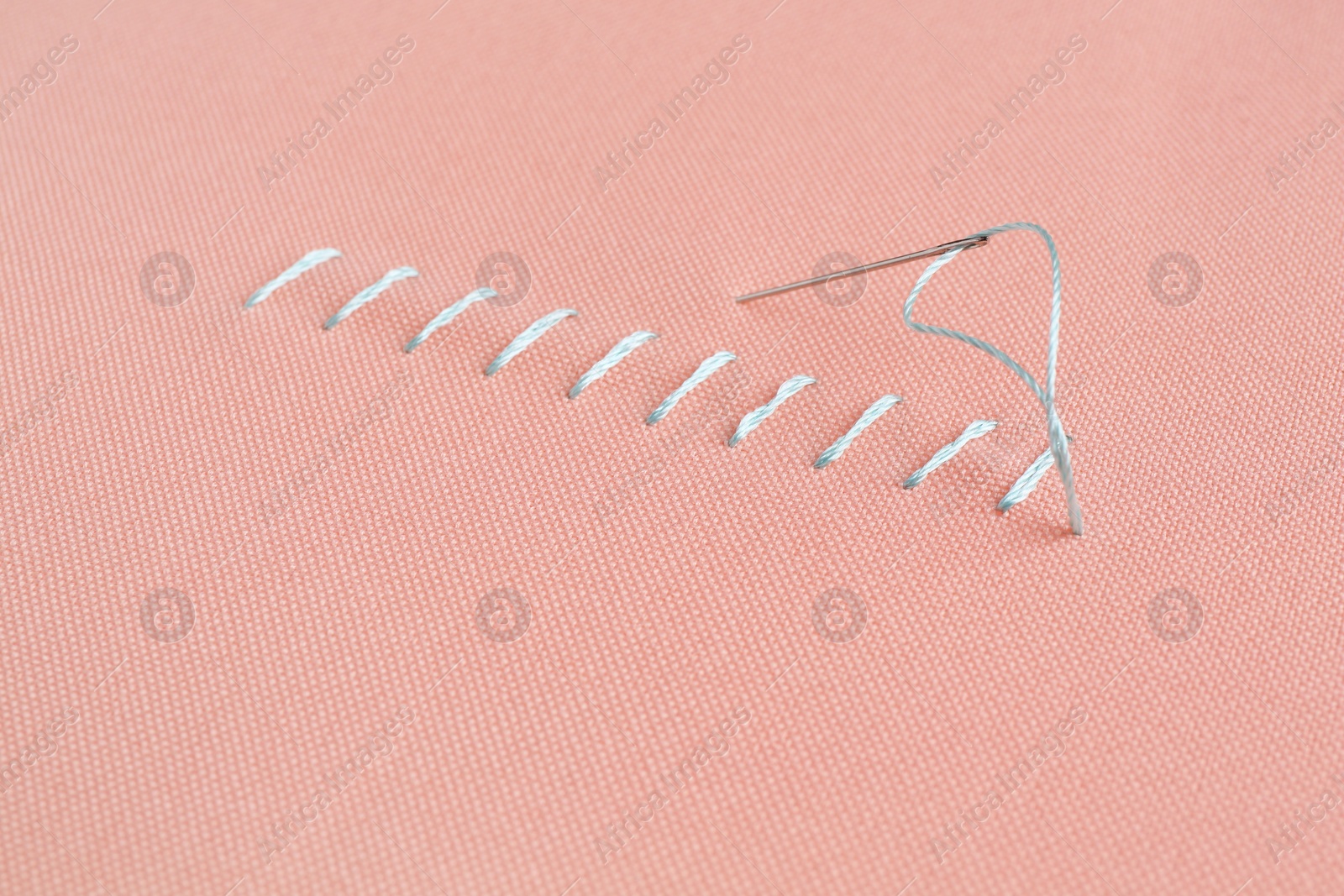 Photo of Sewing needle with thread and stitches on coral cloth, closeup