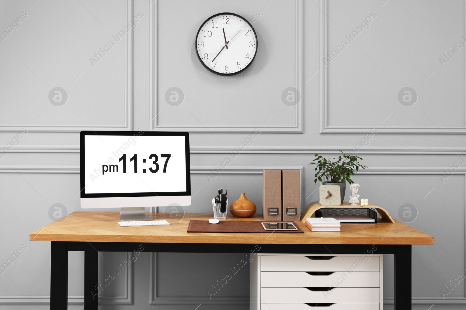 Photo of Stylish workplace with computer, houseplant and stationery on wooden desk near grey wall at home