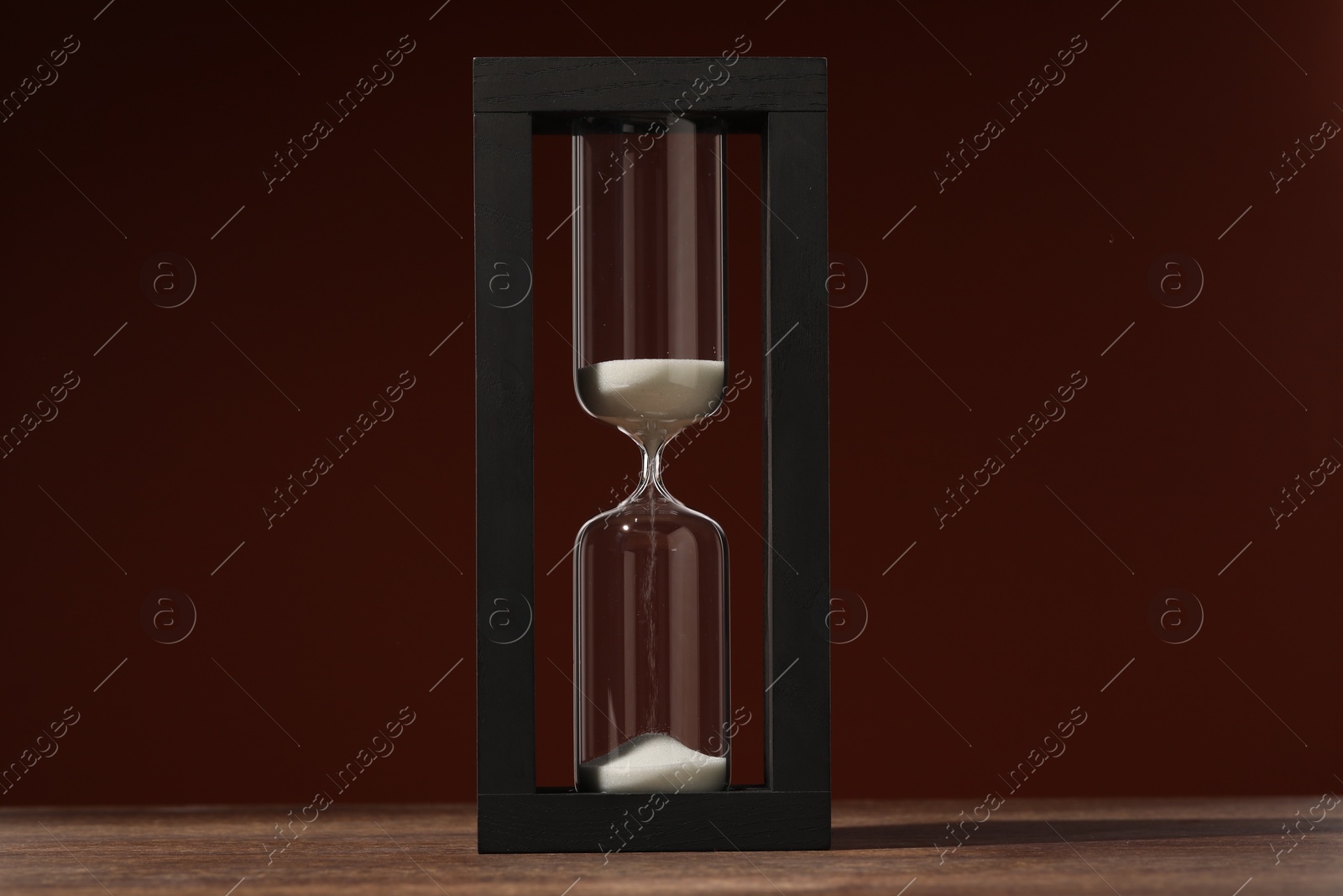 Photo of Hourglass with flowing sand on wooden table against brown background