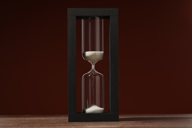 Hourglass with flowing sand on wooden table against brown background