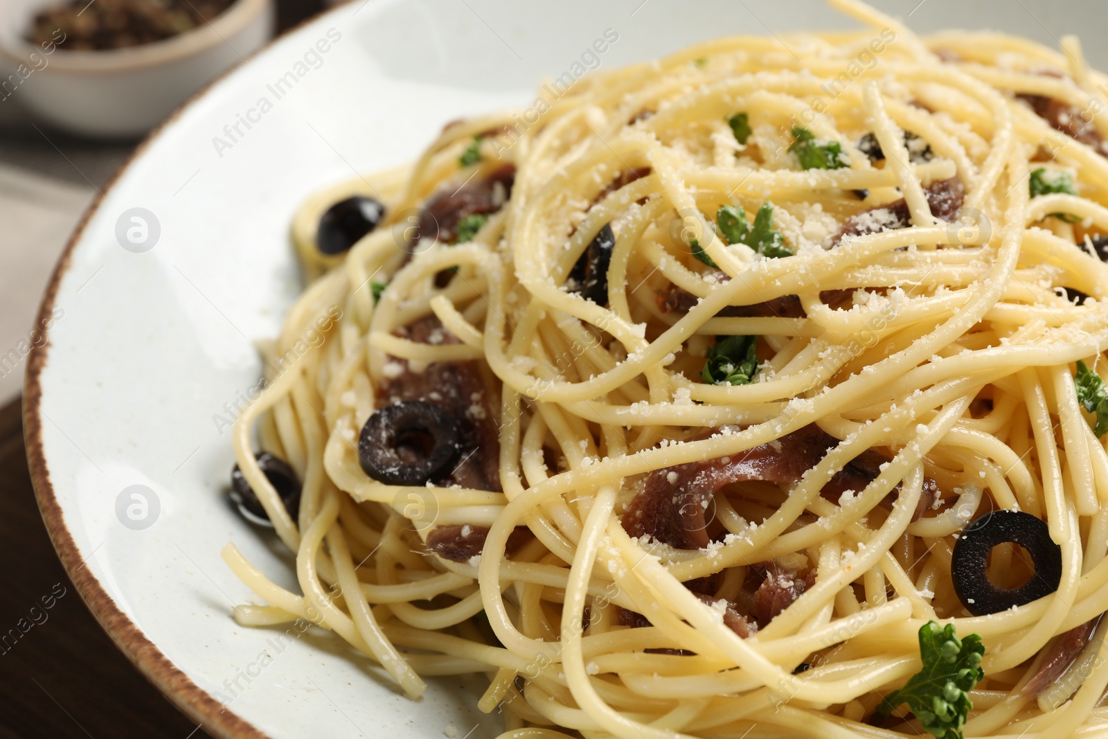 Photo of Delicious pasta with anchovies, olives and parmesan cheese on wooden table, closeup