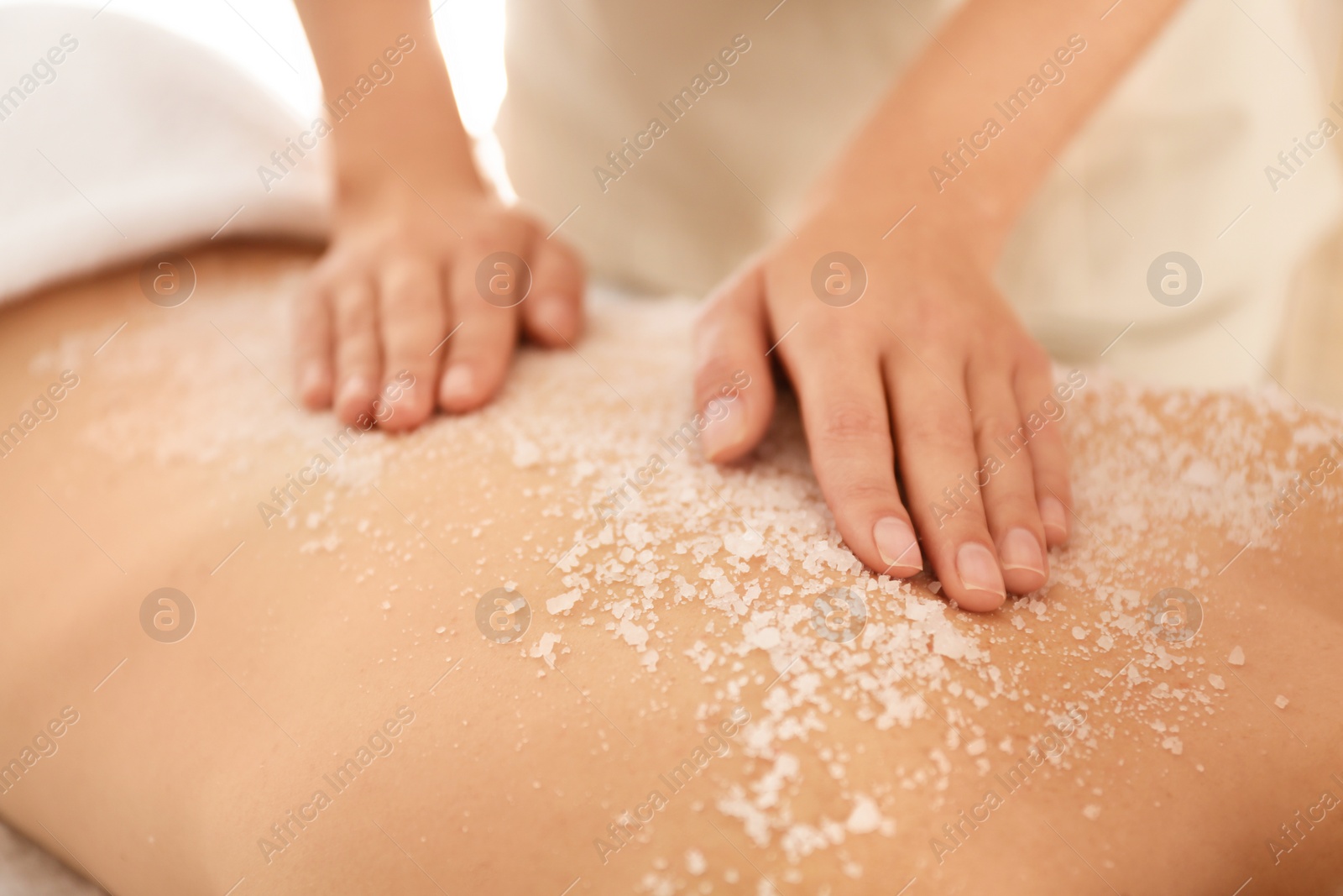 Photo of Young woman having body scrubbing procedure with sea salt in spa salon, closeup