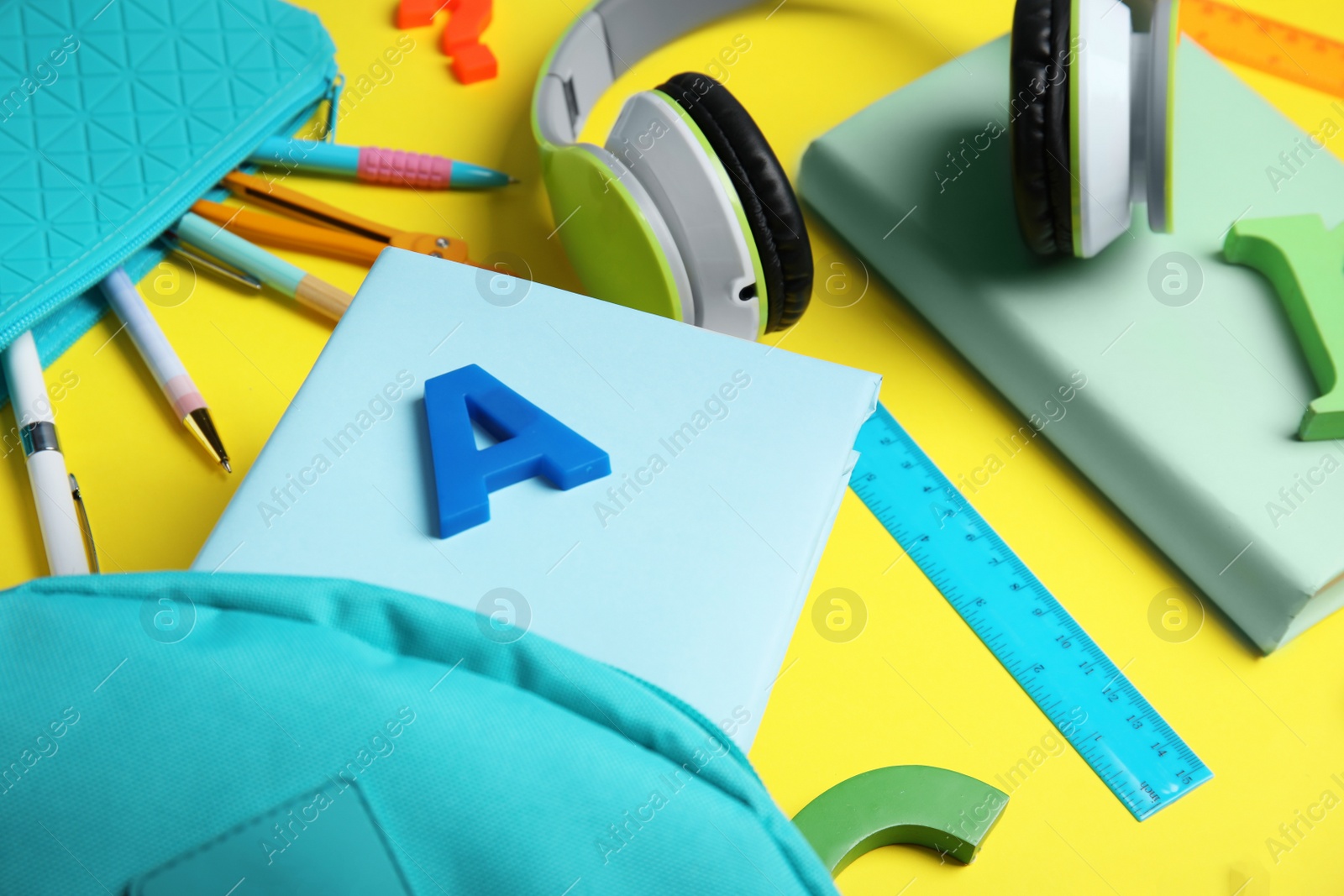 Photo of Books, headphones and school stationery on yellow background