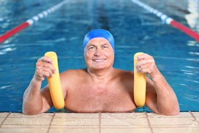 Photo of Sportive senior man with swimming noodle in indoor pool