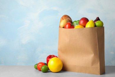 Paper bag with fresh vegetables and fruits on grey table against light background. Space for text