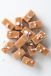 Photo of Tasty caramel candies and salt on white table, top view