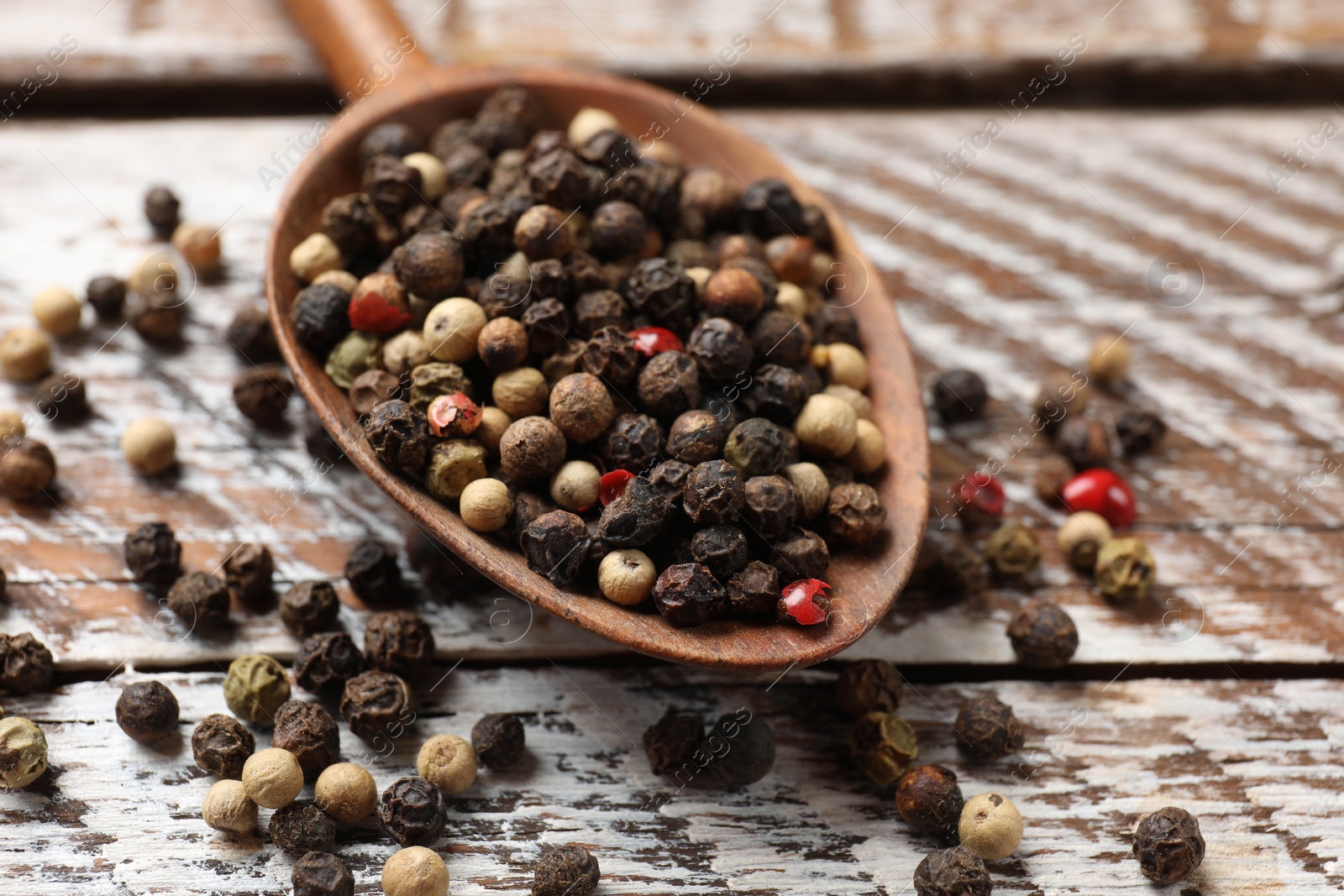 Photo of Aromatic spice. Different peppers in spoon on wooden table, closeup