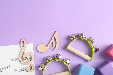 Photo of Tools for creating baby songs. Flat lay composition with wooden notes and tambourines for kids on violet background