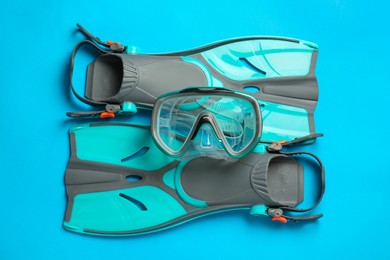 Photo of Pair of turquoise flippers and mask on light blue background , flat lay