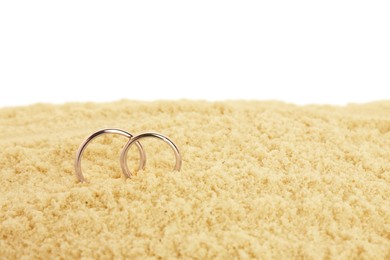 Photo of Honeymoon concept. Two golden rings and sand isolated on white