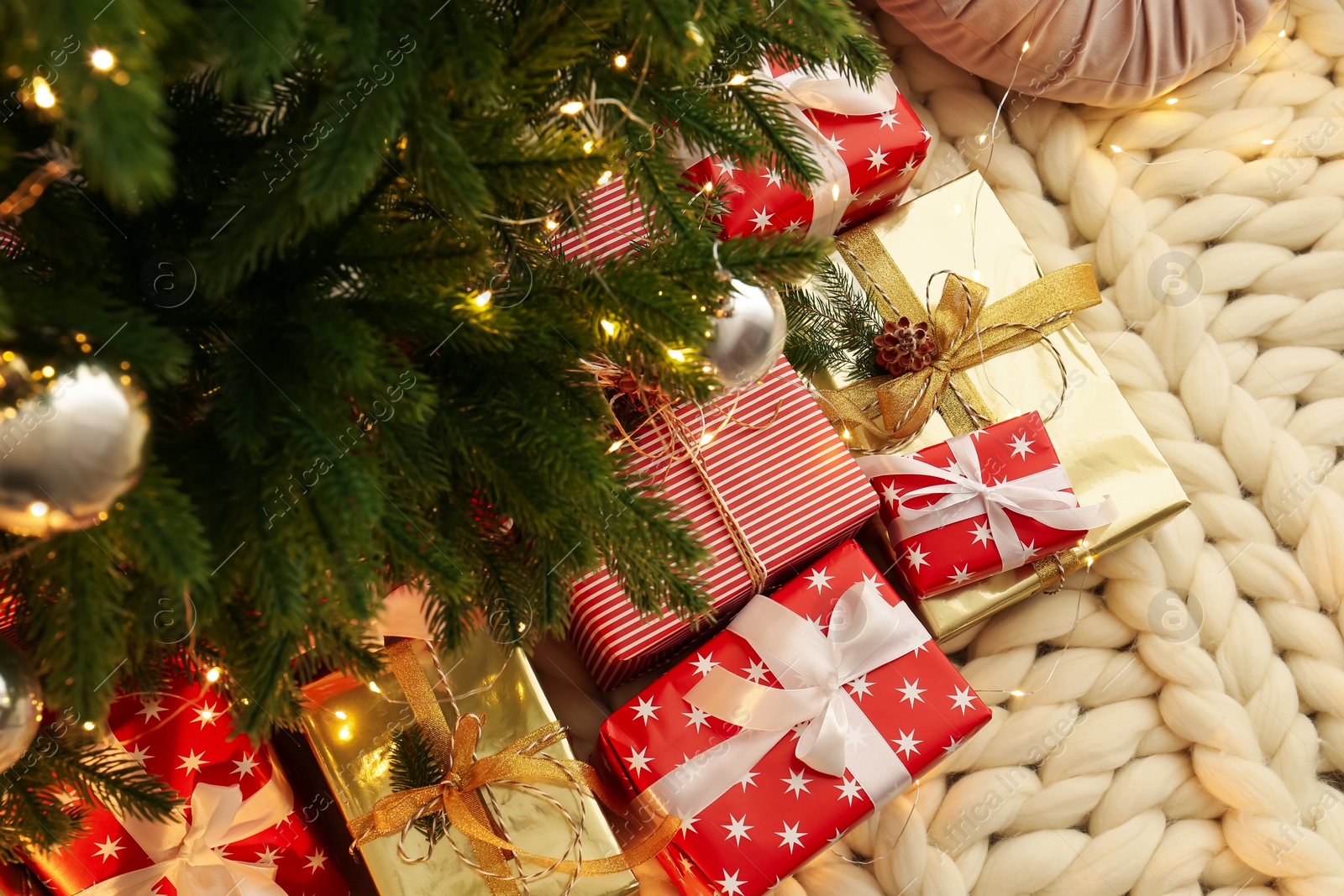 Photo of Pile of gift boxes near Christmas tree on white knitted blanket, above view