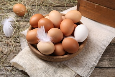 Photo of Fresh chicken eggs in bowl and dried hay on wooden table