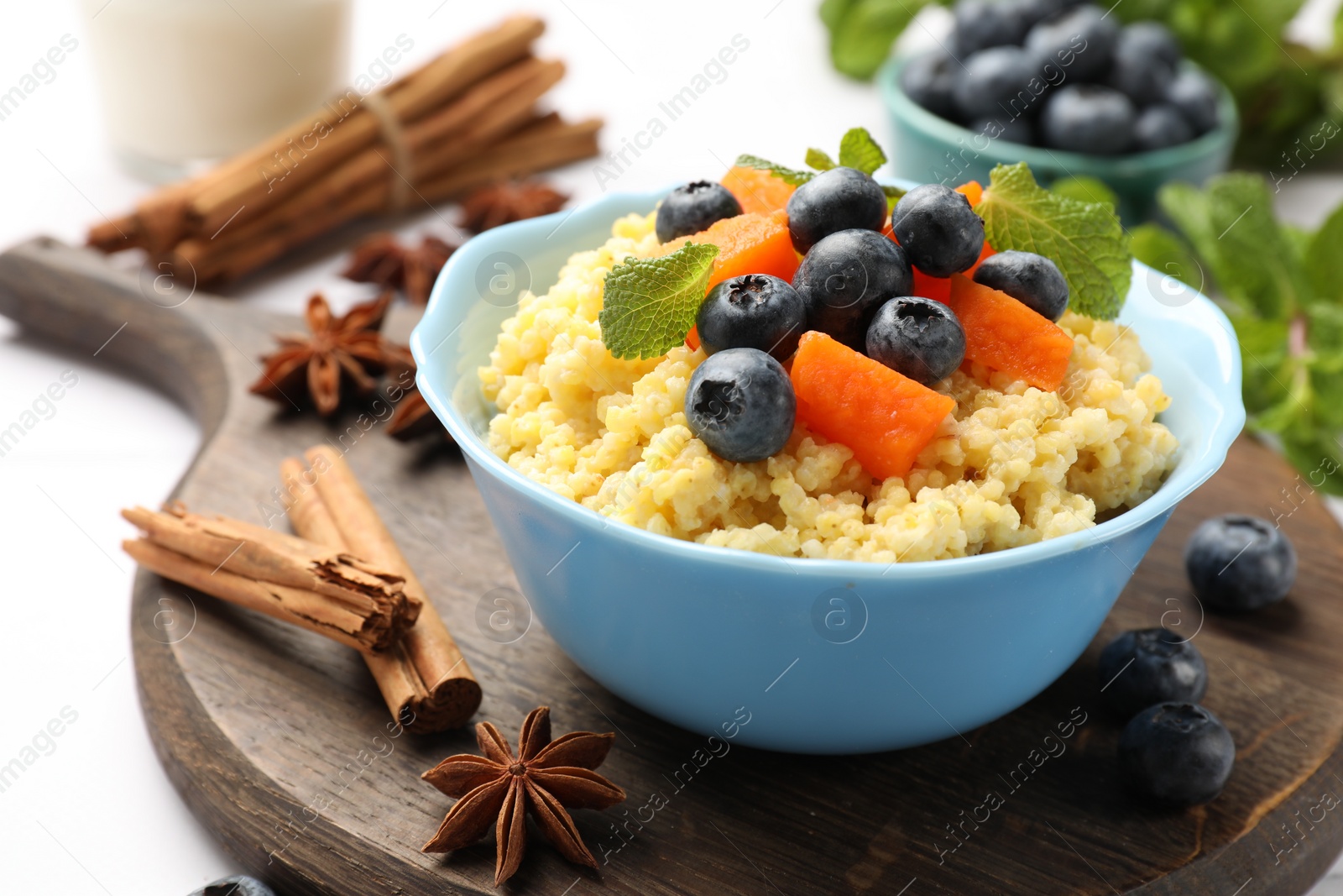 Photo of Tasty millet porridge with blueberries, pumpkin and mint in bowl on white table, closeup