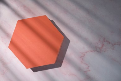 Photo of Orange hexagon on pink marble table, top view with space for text. Stylish presentation for product