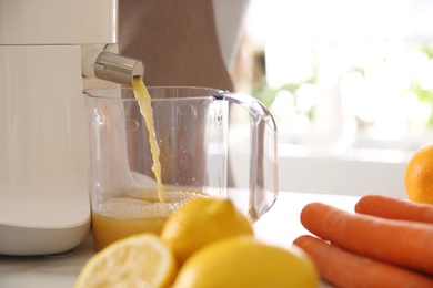 Photo of Modern juicer, fresh fruits and carrots on table in kitchen, closeup