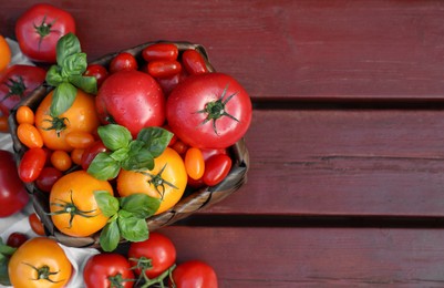 Different sorts of tomatoes with basil on wooden table, above view. Space for text