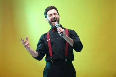 Emotional man with microphone singing on light green background