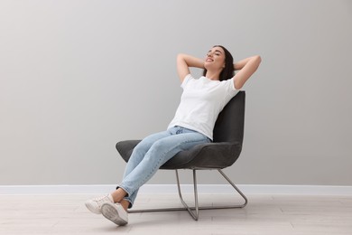 Photo of Beautiful woman relaxing in armchair near light grey wall indoors