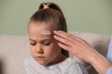 Photo of Mother applying ointment onto her daughter's forehead indoors